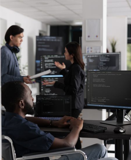 It programmer in wheelchair typing html code in coding office, working on server program with computer. African american web developer with chronic disability writing script with system algorithms.